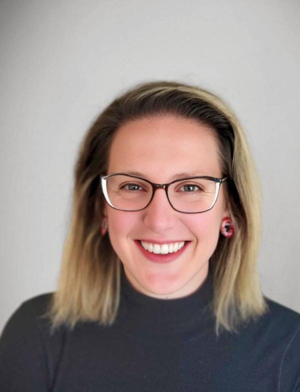 A woman wearing glasses smiling in front of a white background
